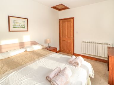 A bedroom with a double bed folded towels on the bed a wooden door a side table with a lamp a radiator and a framed picture on the wall at Swallow Cottage in Milton near Brampton