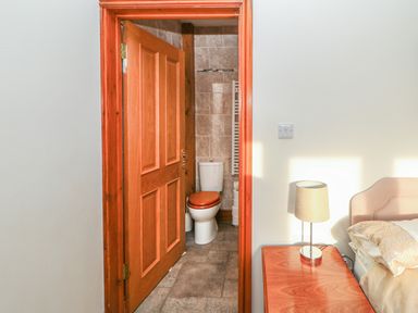 A bedroom with a bedside table lamp and an open wooden door leading to a bathroom with a toilet at Swallow Cottage Milton near Brampton
