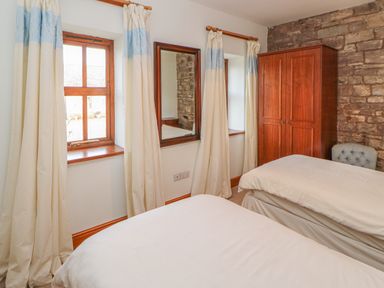 A bedroom with two single beds a wooden wardrobe two windows with curtains and a wall mirror at Swallow Cottage Milton near Brampton