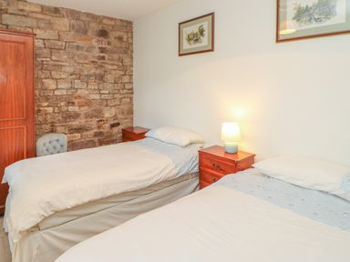 A bedroom with two single beds bedside tables a lamp stone wall and framed pictures at Swallow Cottage in Milton near Brampton