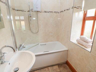 A bathroom with a bathtub shower combo sink and towels on a windowsill at Swallow Cottage in Milton near Brampton