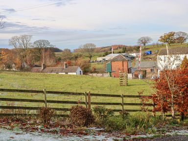 A rural landscape with a wooden fence bushes trees and buildings in the background at Swallow Cottage in Milton near Brampton