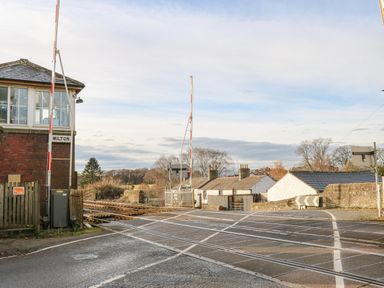 A railway level crossing with barriers and a signal box labeled milton near houses and trees at Swallow Cottage in Milton near Brampton