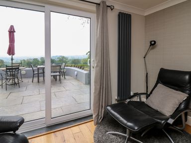 A room with a black leather chair and a small round rug next to sliding glass doors leading to a patio with a table and chairs at Aberdauddwr in Lampeter