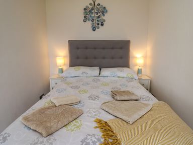A bedroom with a double bed with a gray headboard two bedside tables with lamps and folded towels on the bed at Aberdauddwr in Lampeter