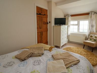 A bedroom with a bed covered in towels a wooden door a white dresser with a television a window with curtains and a chair at Aberdauddwr in Lampeter