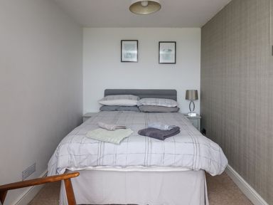 A bedroom with a bed with folded towels on it two framed pictures on the wall and a lamp on a bedside table at Aberdauddwr in Lampeter