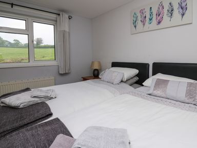 A bedroom with two single beds with white linens and folded towels next to a window at Aberdauddwr in Lampeter