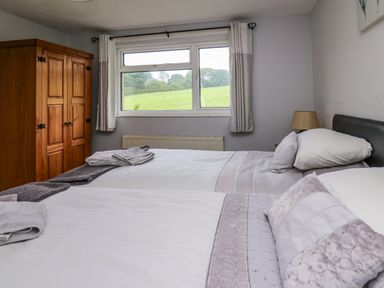 A bedroom with two beds a wooden wardrobe a window with curtains and a view of a field at Aberdauddwr in Lampeter