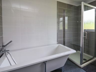 A bathroom with a bathtub and a glass shower enclosure with tiled walls at Aberdauddwr in Lampeter