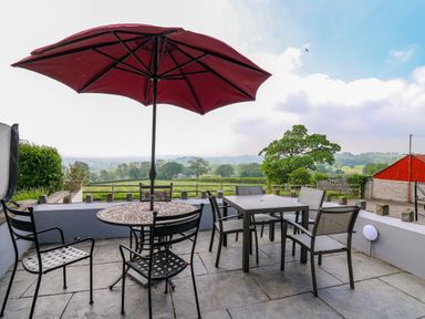An outdoor patio with two tables and chairs with a red umbrella and countryside view at Aberdauddwr in Lampeter
