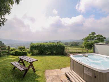 A garden with a hot tub and a wooden picnic table overlooking fields and hills at Aberdauddwr in Lampeter