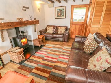 A living room with leather sofas a wood burning stove and a striped rug at Rosemary Cottage in Clawthorpe near Burton-in-Kendal