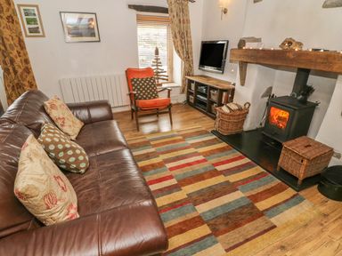 A living room with a leather sofa an armchair a wood burning stove and a patterned rug at Rosemary Cottage in Clawthorpe near Burton-in-Kendal