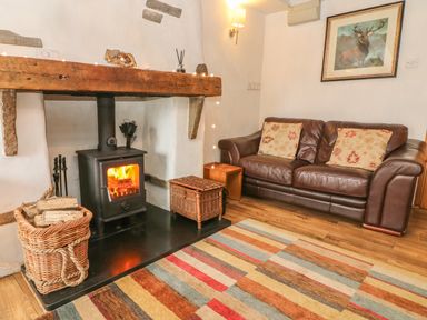A living room with a wood-burning stove basket of logs leather sofa and framed deer picture at Rosemary Cottage in Clawthorpe near Burton-in-Kendal