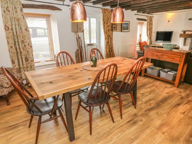 A dining area with a wooden table and six chairs under copper pendant lights at Rosemary Cottage in Clawthorpe near Burton-in-Kendal