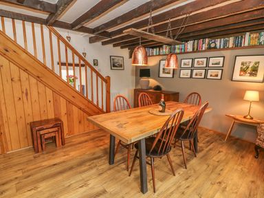 A dining room with a wooden table and chairs under copper pendant lights and books on a shelf at Rosemary Cottage in Clawthorpe near Burton-in-Kendal