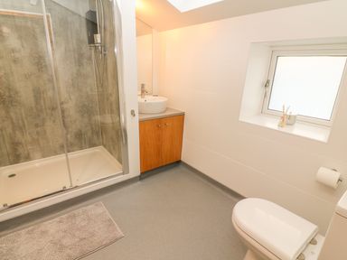 A bathroom with a shower enclosure a sink with wooden cabinet a toilet a window and a bath mat at Rosemary Cottage in Clawthorpe near Burton-in-Kendal