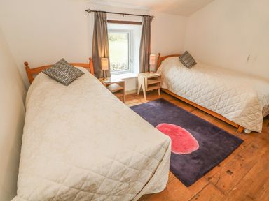 A bedroom with two single beds side by side with nightstands and lamps between them and a window in the center at Rosemary Cottage in Clawthorpe near Burton-in-Kendal