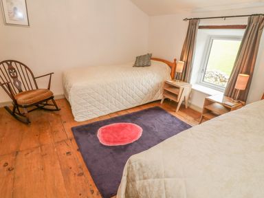 A bedroom with two single beds bedside tables lamps a rocking chair and a window with curtains at Rosemary Cottage in Clawthorpe near Burton-in-Kendal