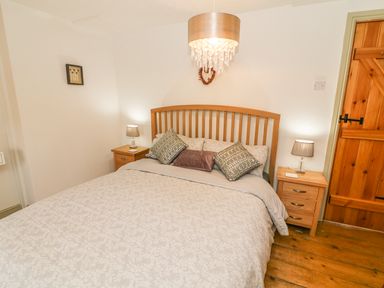 A bedroom with a double bed two bedside tables with lamps a wooden door and a hanging light at Rosemary Cottage in Clawthorpe near Burton-in-Kendal