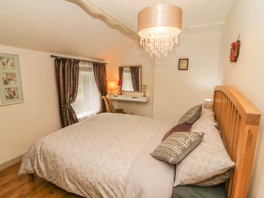 A bedroom with a bed wooden headboard bedside table curtain and a dressing table with a mirror at Rosemary Cottage in Clawthorpe near Burton-in-Kendal