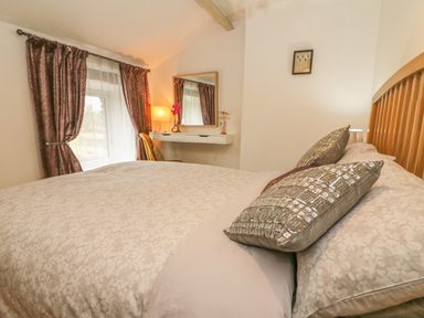 A bedroom with a bed a mirror a desk and curtains at Rosemary Cottage in Clawthorpe near Burton-in-Kendal