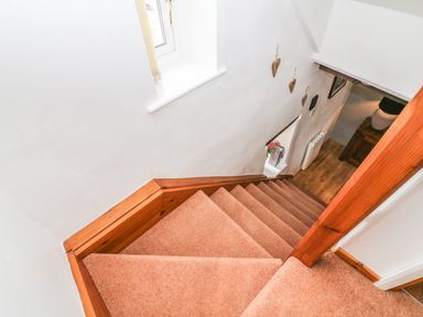 Carpeted staircase with wooden trim and white walls with window and heart-shaped decorations at Rosemary Cottage in Clawthorpe near Burton-in-Kendal