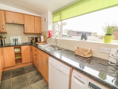 A kitchen with wooden cabinets a double sink a dishwasher a washing machine and various kitchen items on the countertop at Rosemary Cottage in Clawthorpe near Burton-in-Kendal