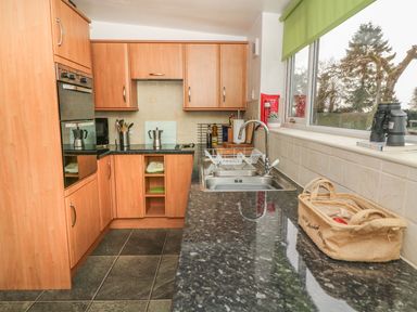 A kitchen with wooden cabinets a black countertop a double sink and a large window at Rosemary Cottage in Clawthorpe near Burton-in-Kendal