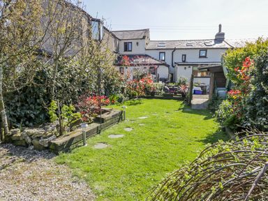 A garden with a lawn pathway plants and a house in the background at Rosemary Cottage in Clawthorpe near Burton-in-Kendal