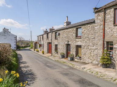 A street with stone cottages and potted plants alongside a narrow road at Rosemary Cottage in Clawthorpe near Burton-in-Kendal
