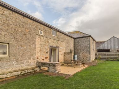 Stone building with small windows and patio with picnic table next to grass at Mill House in Lowick