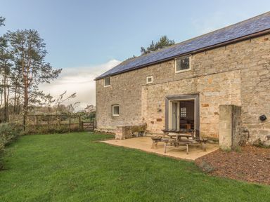 A stone building with a tiled roof and outdoor picnic table on a patio surrounded by grass at Mill House in Lowick