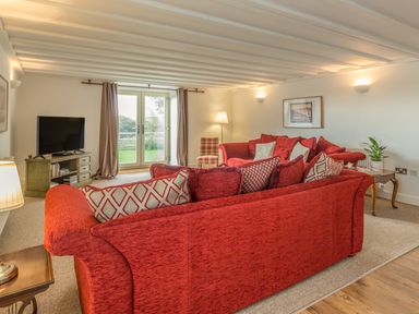 A living room with red sofas a television on a stand and glass doors at Mill House in Lowick
