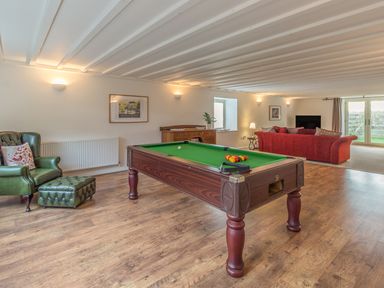 A room with a pool table a green leather armchair and ottoman a red sofa a wooden sideboard a television and a door to a garden at Mill House in Lowick