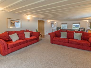 A living room with two red sofas with cushions a wooden side table two armchairs and a pool table at Mill House in Lowick