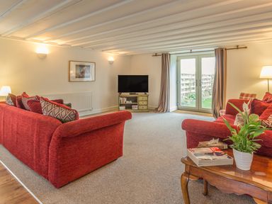 A living room with red sofas a television on a stand and French doors at Mill House in Lowick