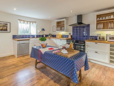 A kitchen with a wooden table covered with a blue and white polka dot cloth and utensils at Mill House in Lowick