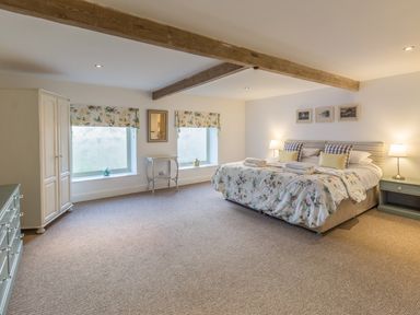 A bedroom with a double bed floral bedding wooden beams two windows with floral blinds and bedside lamps at Mill House in Lowick