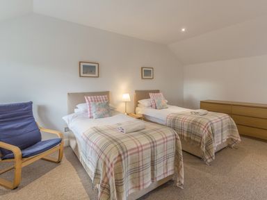 A bedroom with two single beds with plaid blankets and pillows a wooden chair and a wooden dresser at Mill House in Lowick