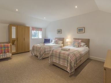 A bedroom with two single beds a wardrobe a crib and a window at Mill House in Lowick