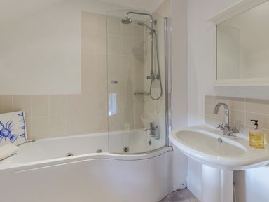 A bathroom with a bathtub shower combination and a sink with a mirror at Mill House in Lowick