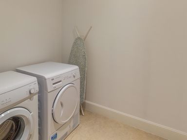 A laundry room with a washing machine dryer and an ironing board at Mill House in Lowick