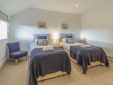 A bedroom with two single beds a chair a lamp and framed pictures at Mill House in Lowick