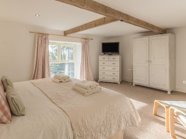 A bedroom with a bed television chest of drawers wardrobe and window at Mill House in Lowick