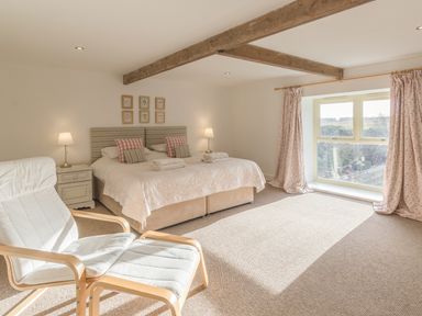 A bedroom with a double bed two bedside tables lamps a window with curtains and a padded chair with footrest at Mill House in Lowick