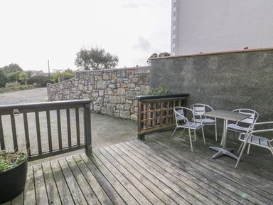An outdoor wooden deck with metal chairs and a table next to a stone wall at Bryn Y Don Cottage in Benllech