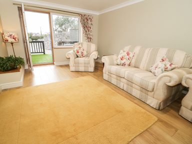 A living room with a sofa armchair a floor lamp and a door opening to an outdoor stone wall at Bryn Y Don Cottage in Benllech