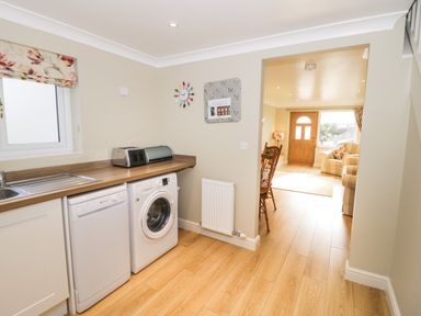 A kitchen area with a dishwasher washing machine and toaster leading to a living room at Bryn Y Don Cottage in Benllech